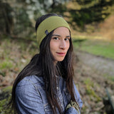 BAsic Sportstirnband in pistaziengrün aus 100% Biobaumwolle, Frau mit langen dunkelbraunen Haaren und Jeanshemd im Wald, schaut in die Kamera.