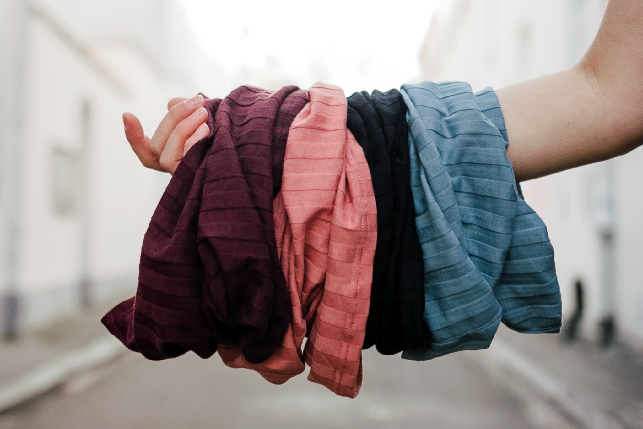 Bio Baumwoll Loops in 4 Farben, weinrot, altrosa, schwarz und graublau auf einem Arm gehalten